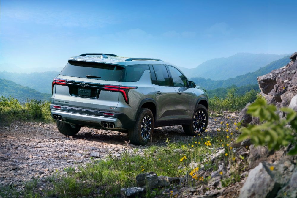 Passenger-side rear 3/4 view of 2024 Chevrolet Traverse Z71 in Sterling Gray Metallic parked on a gravel road with forested hills in the background