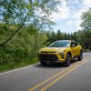Front 3/4 view of 2024 Chevrolet Trax ACTIV in Nitro Yellow Metallic driving on a road lined with trees