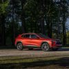 Passenger’s side 7/8 view of 2024 Chevrolet Trax LT in Cayenne Orange Metallic parked on a gravel road in front of trees