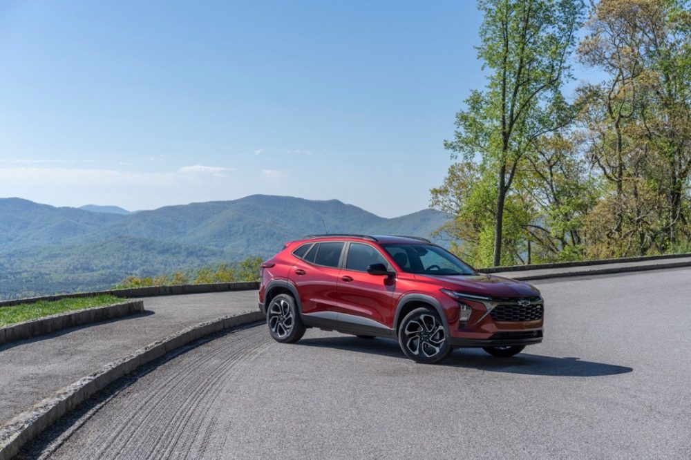 Front 3/4 view of 2024 Chevrolet Trax 2RS in Crimson Metallic parked on a road with mountains in the background