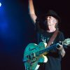 During a 2014 concert, Neil Young raises one hand while grasping the neck of his guitar with the other