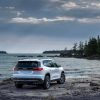 A rear 3/4 view of the 2024 GMC Acadia AT4 parked on the rocky, wooded shore of a lake