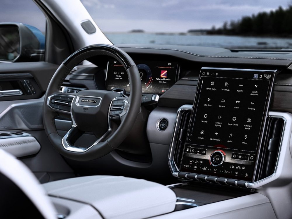 An interior view of the 2024 GMC Acadia Denali that shows the SUV's steering wheel and 15-inch portrait-oriented touchscreen