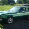 A green AMC Gremlin parked in a rural home area