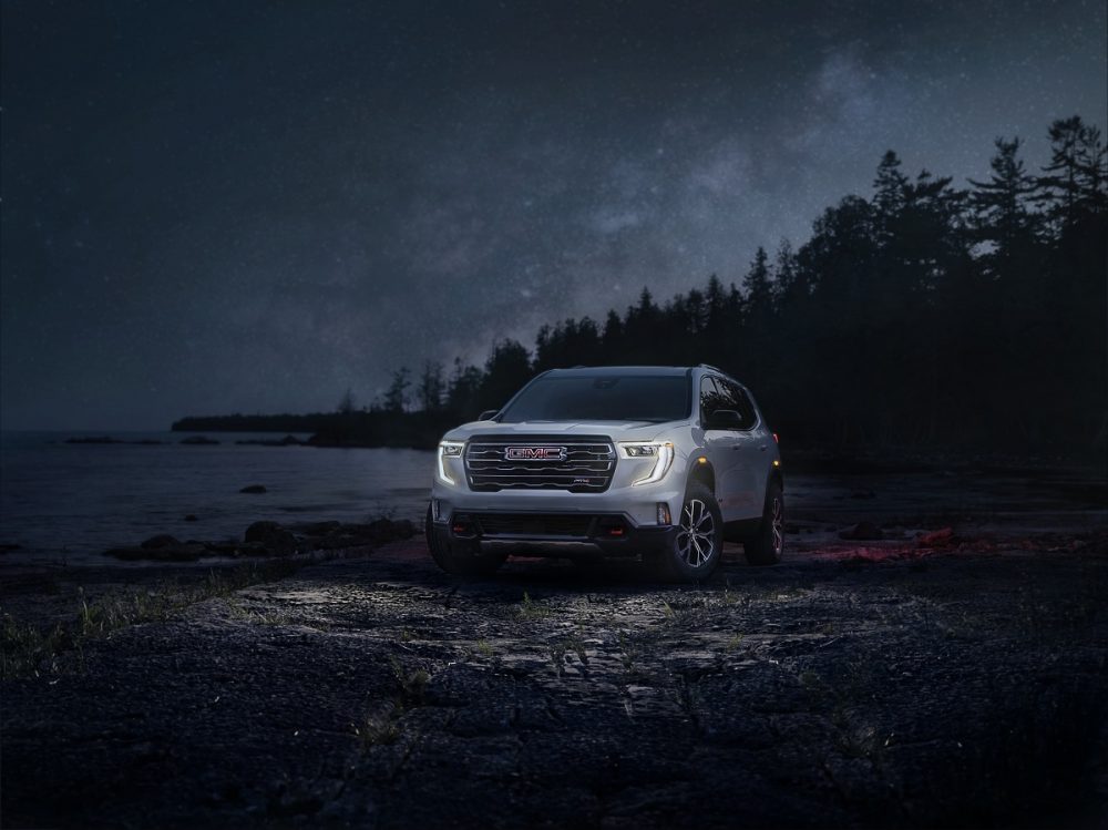 Front 3/4 shot of a white 2024 GMC Acadia AT4 parked in front of a lake at night