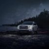 Front 3/4 shot of a white 2024 GMC Acadia AT4 parked in front of a lake at night