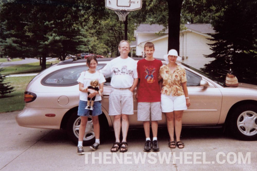 Family standing next to tan Ford Taurus station wagon vehicle