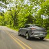 Rear 3/4 view of gray 2024 Buick Envista Avenir driving on tree-lined road