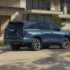 Rear ¾ view of the 2025 Cadillac Escalade Sport Platinum in Deep Sea Metallic with a house and greenery in the background.