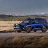 A blue 2025 Subaru Forester parked on a gravel road with fields and mountains in the background