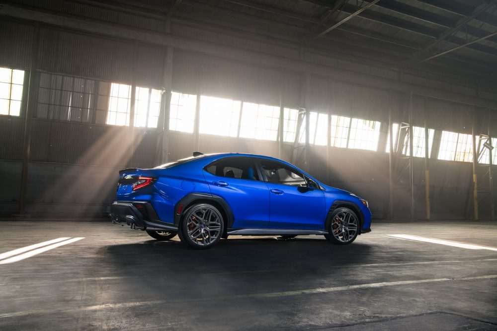 A rear profile view of a blue 2025 Subaru WRX tS posed inside an industrial building with light shining through the windows