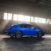 A rear profile view of a blue 2025 Subaru WRX tS posed inside an industrial building with light shining through the windows