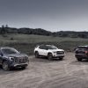 The 2026 GMC Terrain Denali, 2026 Terrain AT4, and 2025 Terrain Elevation are parked next to each other on a gravel lot with a field and trees in the background