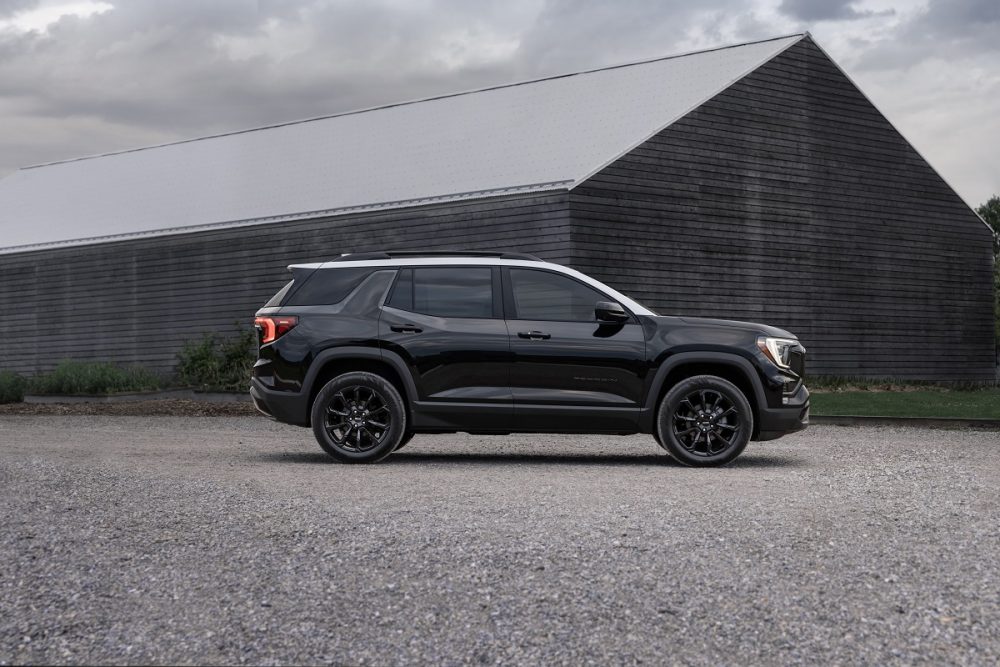 A next-generation 2025 GMC Terrain Elevation with a gray two-tone roof is shown in side profile in front of a barn