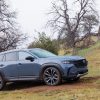 A side view of the 2025 Mazda CX-50 driving up a muddy, tree-studded hill in the rain