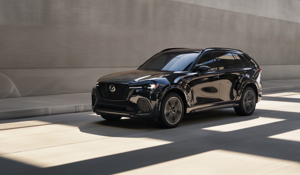 A front side view of a black 2025 Mazda CX-70 driving through shadows