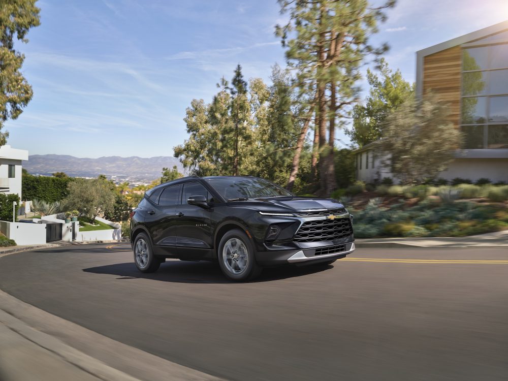 Front 3/4 view of the 2025 Chevrolet Blazer 3LT in Black, driving in front of a home.