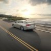 Rear 3/4 view of the 2024 Chevrolet Malibu driving near a body of water with the sun low in the sky