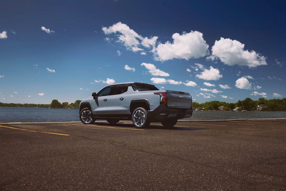 A rear 3/4 view of a Slate Gray 2025 Chevrolet Silverado EV LT parked under a blue sky with fluffy white clouds