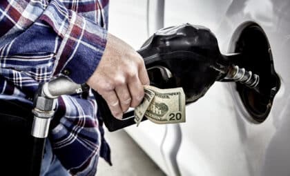 Man's hand holding forty dollars cash and gas nozzle while pumping gas into parked vehicle