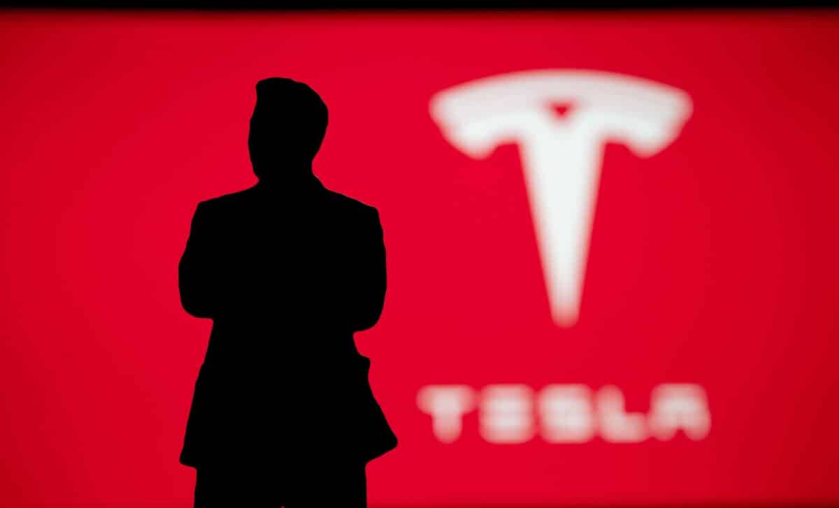 Silhouette of Elon Musk on Tesla presentation, company logo on red background