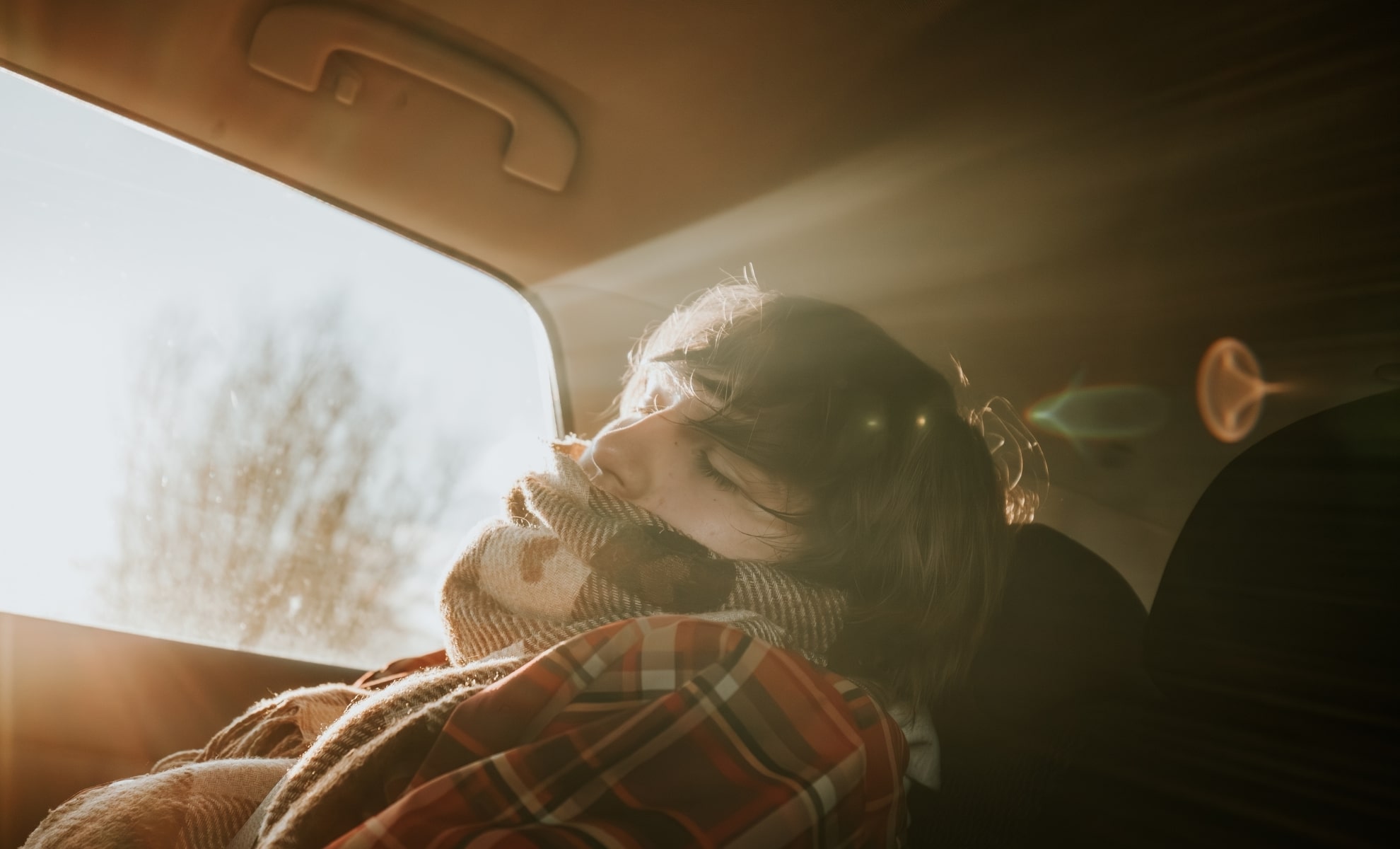 A passenger, wrapped in a blanket, sleeps in a car